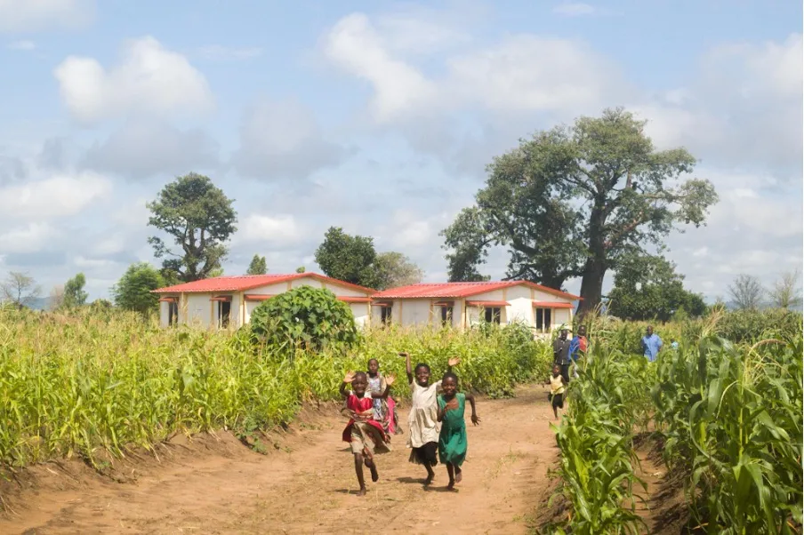 An image of children running and smiling outside of a new home in Phalombe Malawi